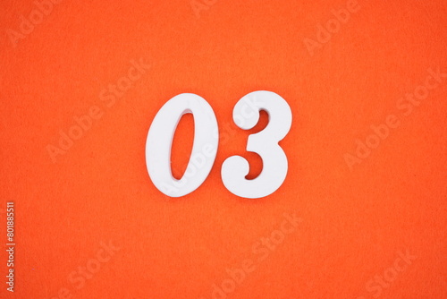 The number 03 is made from white painted wood placed on a background of orange paper.