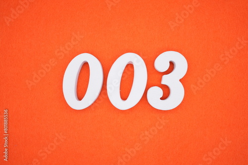 The number 003 is made from white painted wood placed on a background of orange paper.