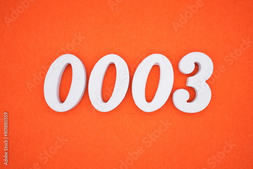 The number 0003 is made from white painted wood placed on a background of orange paper.