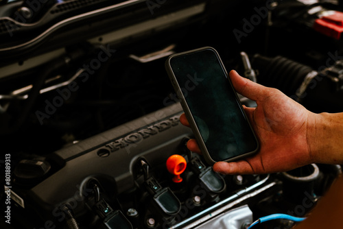 Mechanic uses smartphone to inspect car engine parts