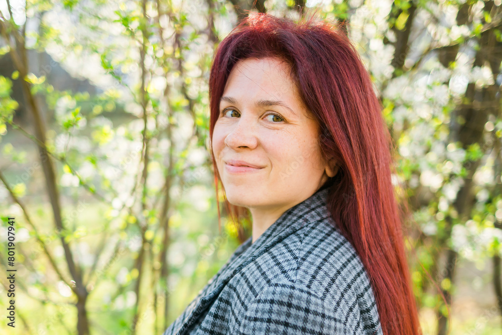 Beautiful red-haired woman enjoying smell in a flowering blooming spring garden. Spring blossom. Copy space and empty place for advertising text Beautiful red-haired woman enjoying smell in a flowering blooming spring garden. Spring blossom. Copy space and empty place for advertising text