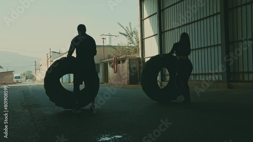 Woman and man do crossfit outside and flip tires camera moves to side