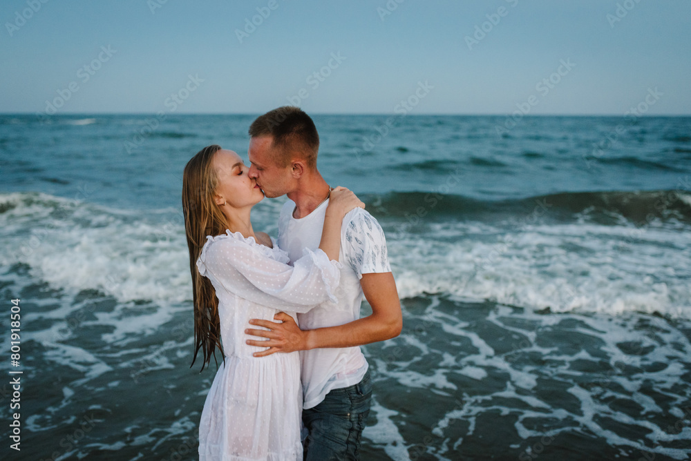 Swimming in clothes. Portrait of a beautiful man and woman wet in sea. Couple hugging and kissing in sea. Male kisses and hugs female standing on water with big waves ocean and enjoying a summer day. Swimming in clothes. Portrait of a beautiful man and woman wet in sea. Couple hugging and kissing in sea. Male kisses and hugs female standing on water with big waves ocean and enjoying a summer day.