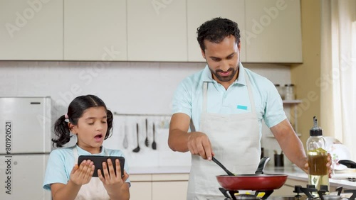 Father cooking for daughter by watching cooking video on mobile phone at kitchen - concept of fatherhood, modern lifestyle and childhood memories