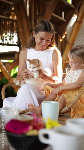 Mother and cild having breakfast in bamboo house tropical resort and playing with cat photo