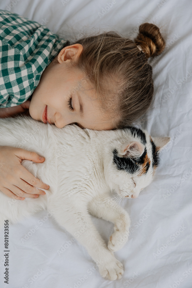 a cute 6-year-old girl fell asleep sweetly next to a fluffy cat on her bed. Child with cat sleep on the white bed a cute 6-year-old girl fell asleep sweetly next to a fluffy cat on her bed. Child with cat sleep on the white bed