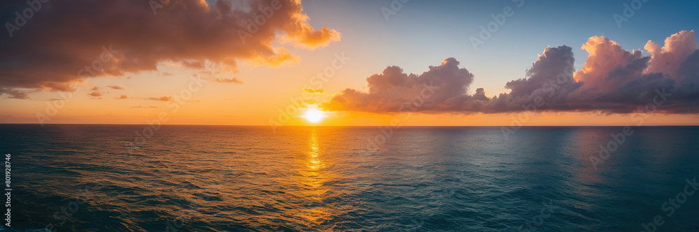 beautiful sunset over a calm sea. The sun is near the horizon, casting a warm glow on the clouds above. The waves are gentle, and the sky is a mix of orange, yellow, and blue. The whole scene has a se