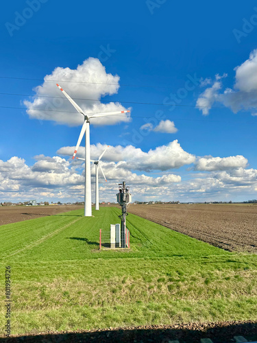 Agricultural field surrounded by Windmills with high wind turbines for generation electricity with power lines and railways. Green energy concept. Wind power production
