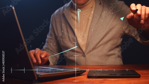 A businessman working on a laptop and graphics tablet models graphics in space on a coordinate system. Concept of modern startup and financial success. Cg