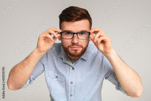 Young redhaired guy try on glasses in front of camera on studio background  panorama