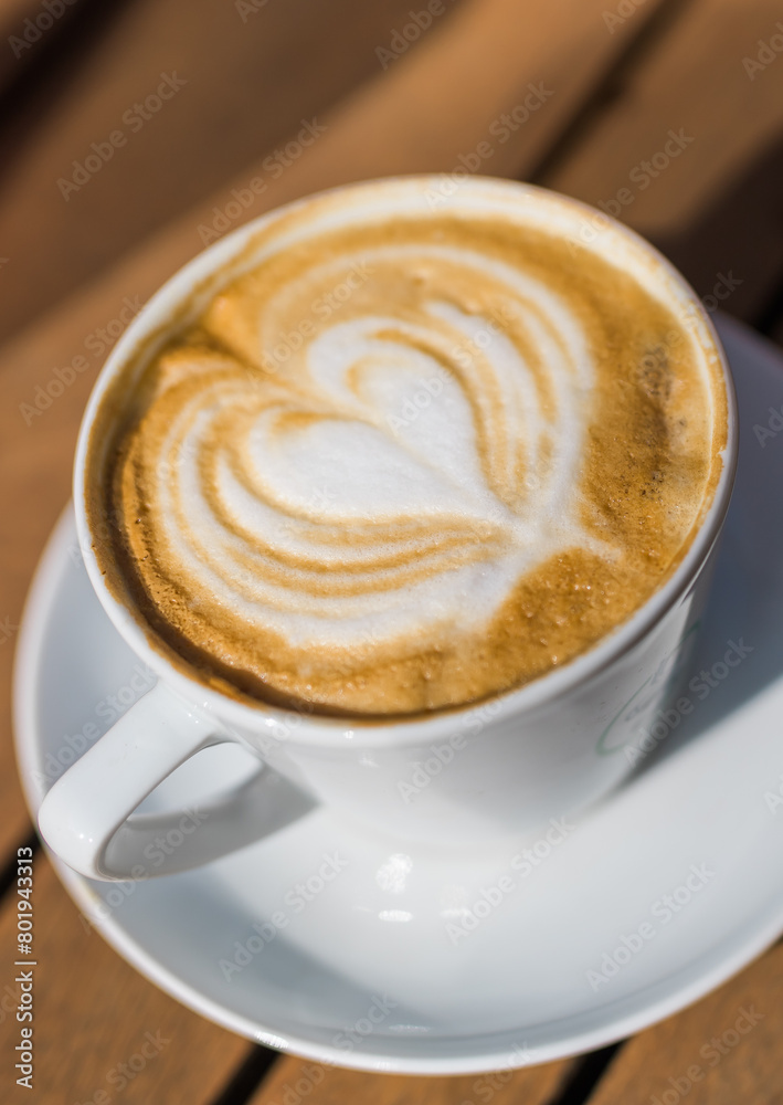 Coffee on wooden background. Cup of cappuccino with latte art on brown table with sunbeam. Fresh morning coffee with delicious milk foam. Coffee on wooden background. Cup of cappuccino with latte art on brown table with sunbeam. Fresh morning coffee with delicious milk foam.