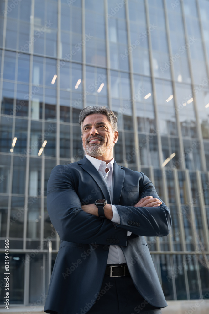 Smiling confident latin hispanic mature business man standing crossed arms. Vertical portrait older senior businessman professional ceo, manager, leader looking aside near office building background Smiling confident latin hispanic mature business man standing crossed arms. Vertical portrait older senior businessman professional ceo, manager, leader looking aside near office building background