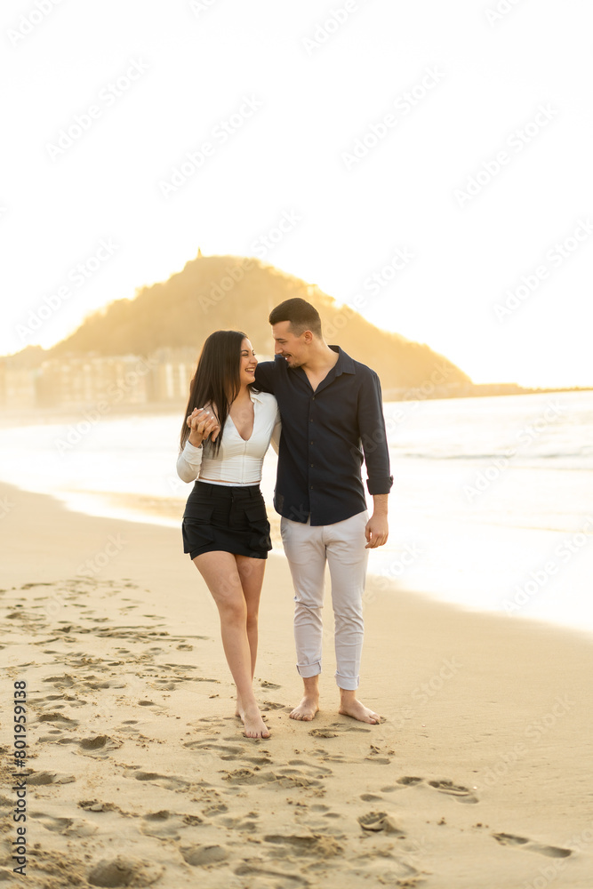 Romantic young couple walking embraced barefoot along a beach Romantic young couple walking embraced barefoot along a beach
