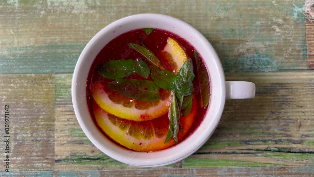 Beautiful top view of a white cup with fruit tea. Red fruit tea, a couple of slices of lemon. There is tea and mint leaves in a cup. Beautiful top view of a white cup with fruit tea. Red fruit tea, a couple of slices of lemon. There is tea and mint leaves in a cup.