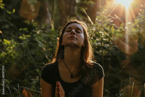 Woman in black shirt meditating in a forest with sun shining through her eyes photo