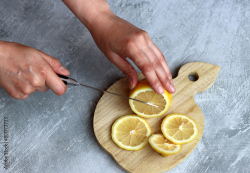 Female hands cut lemons on a wooden board on a gray background with space for text