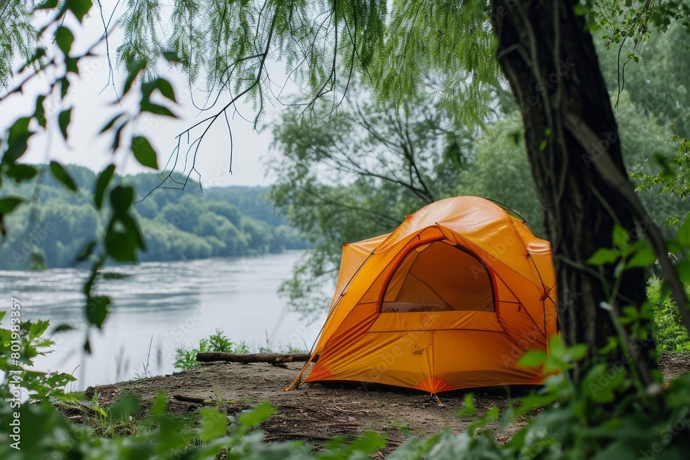 A bright tent in the forest on the bank of a river against the backdrop of mountains. Concept of tourism, vacation, travel, hiking