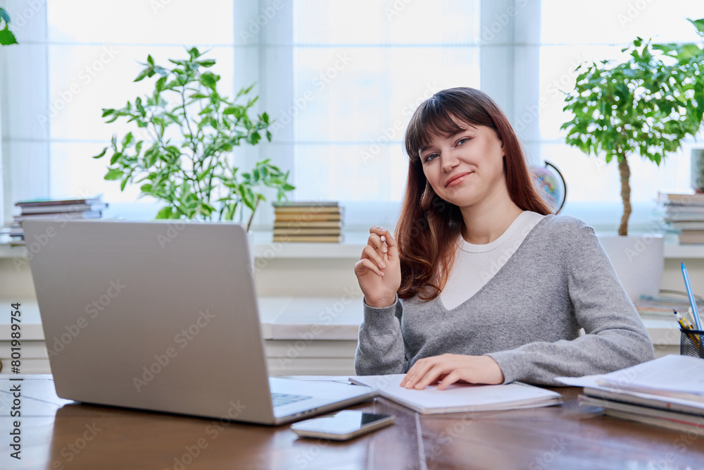 Young female college student studying at home using laptop, looking at camera Young female college student studying at home using laptop, looking at camera