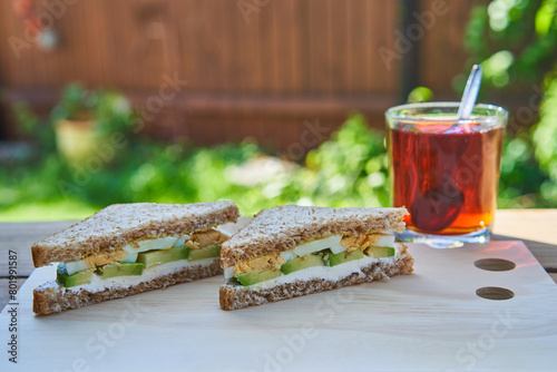 Simple, healthy and light breakfast with balanced nutritions served outside in the home garden during sunny summer morning. Meal constist from wholegrain sandwich with avocado and egg slices and tea.