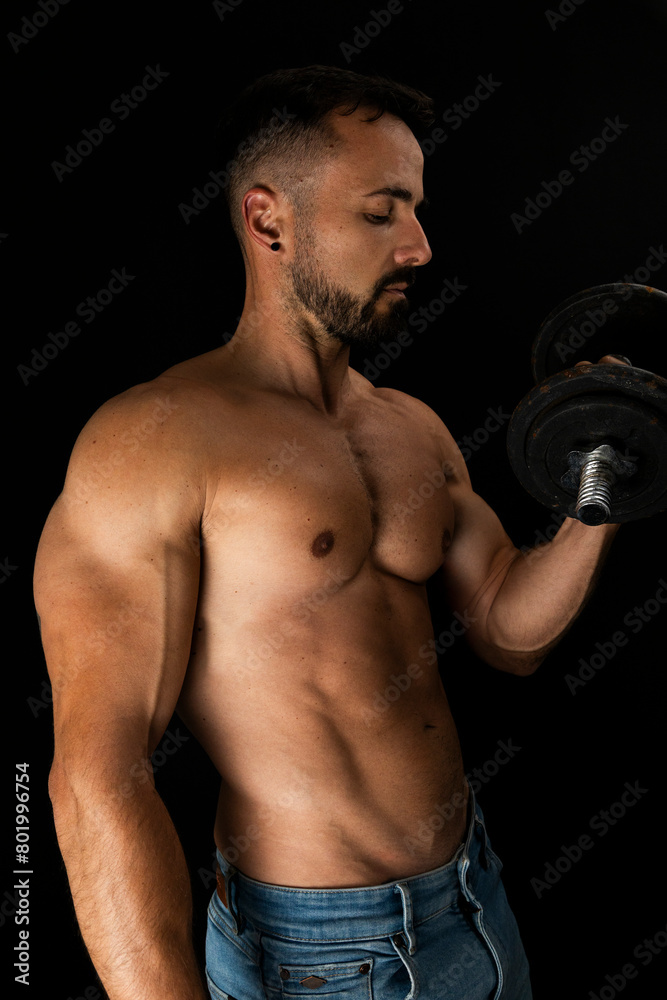 Strong shirtless man doing shoulder presses with dumbbell in photo studio