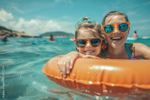 Mother and daughter in sunglasses with inflatable ring at beach, having fun on summer vacation