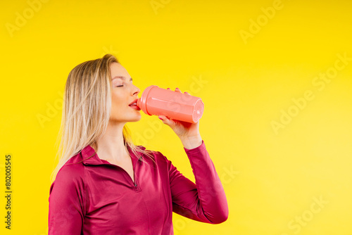 Happy beautiful brunette woman with water bottle or proteine shake on yellow background