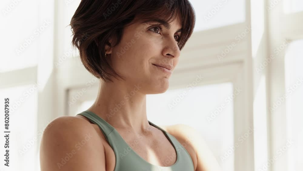 Closeup side view of a brunette woman smiling gently while practicing yoga, exuding calmness in a bright studio space. Closeup side view of a brunette woman smiling gently while practicing yoga, exuding calmness in a bright studio space.