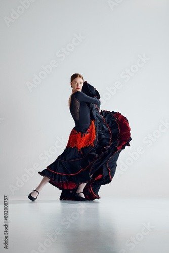 Captivating flamenco performance. Passionate and artistic woman in elegant dress dancing traditional Spanish dance against grey studio background. Concept of art of movement, classical dance, beauty