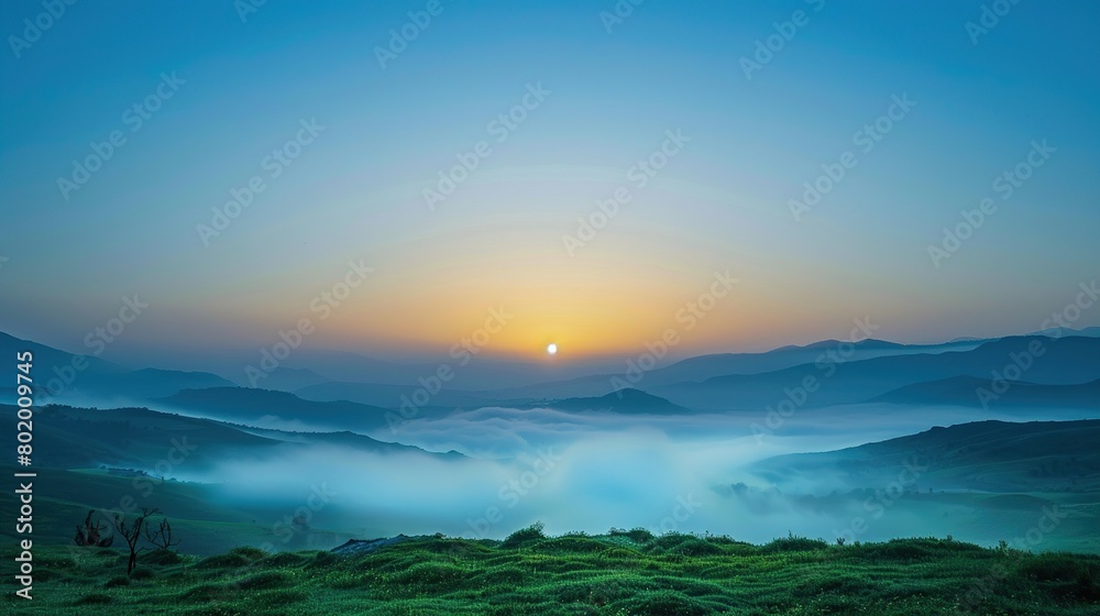 a foggy landscape. The foreground is a green grassy field with some yellow flowers. In the background are hills and trees covered in a thick white fog. 