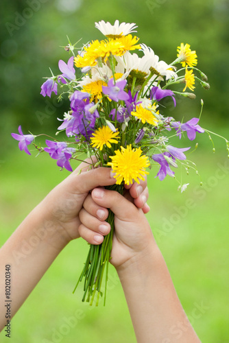 Children holding a bouquet of meadow flowers. Blurred green background