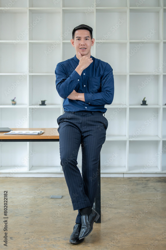 Young Asian male professional stands thoughtfully in a stylish office setting, dressed in business attire. Young Asian male professional stands thoughtfully in a stylish office setting, dressed in business attire.
