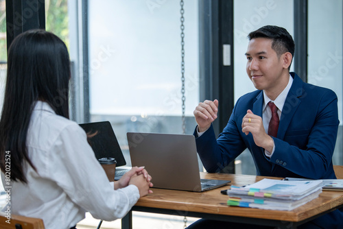 Two Asian professionals engaging in a thoughtful discussion at a business meeting, with a laptop and documents on the table.