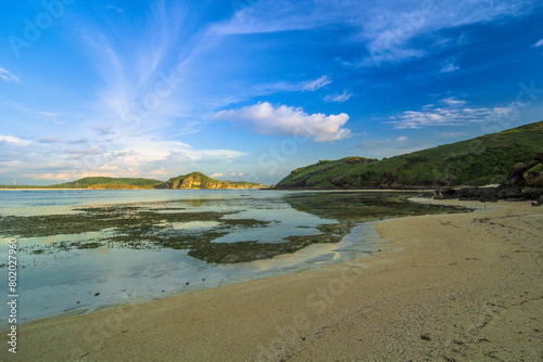 the view of the vast blue sea with white sand and the edge of the sea water there is sea grass growing with the blue sky and thin white clouds on Tanjung Aan beach