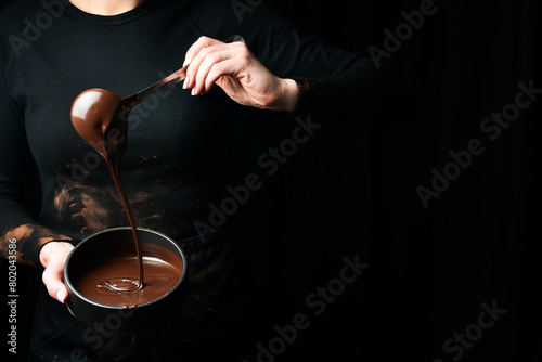 The chef scoops hot chocolate into a bowl. On a black background. Preparation of chocolate. photo