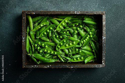 Pods of green peas with leaves in a wooden box. On a black stone background. Top view. Healthy food. © Yaruniv-Studio