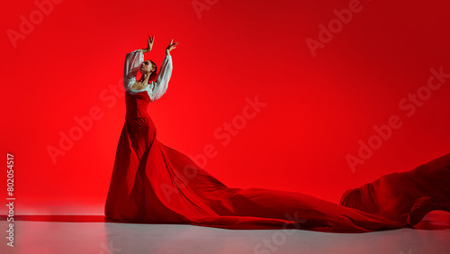 Intensity of flamenco dance. Creative artistic performance, elegant female dancer in bright costume dancing against red background. Concept of art of movement, classical dance, beauty, festival