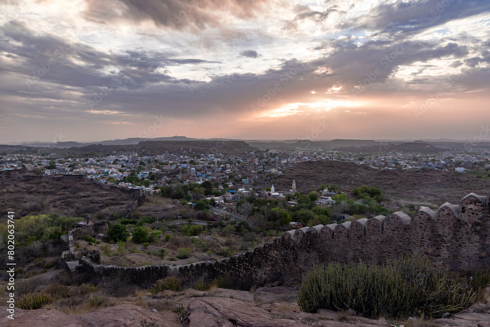 city view with dramatic sun beams orange sky and ancient fort wall at evening from mountain top