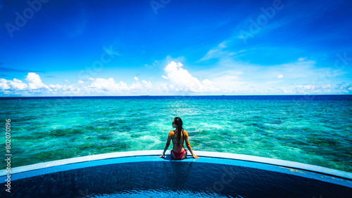Woman on edge of a pool over Maldive Lagoon - clear blue sky