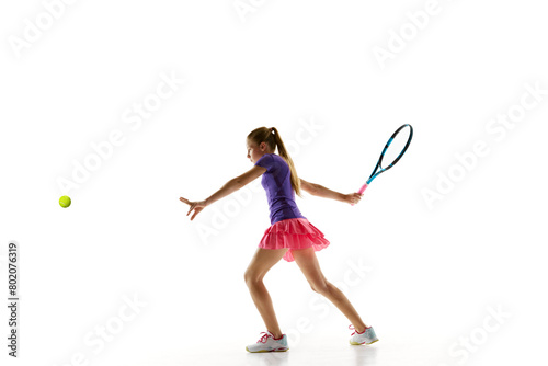 Dynamic portrait of athletic teenage girl taking passing shot to opponent in motion against white studio background. Concept of professional sport, movement, tournament, action. Ad © Lustre