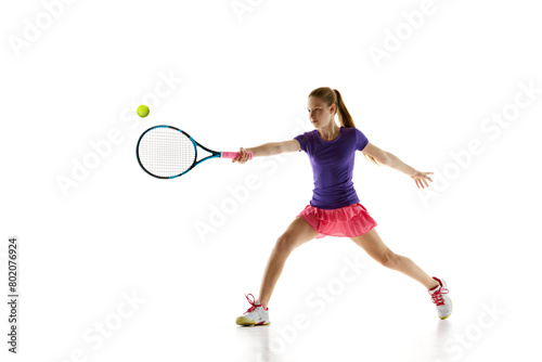 Tennis skills. Dynamic portrait of athletic teenage girl perfectly serving ball to opponent in motion against white studio background. Concept of professional sport, movement, tournament, action. Ad © Lustre