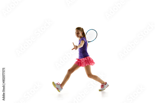 Athletic teenage girl, tennis player in uniform ready to accept opponent's serve in motion against white studio background. Concept of professional sport, movement, tournament, action. Ad