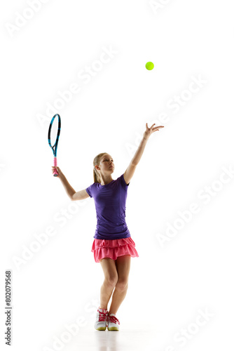 Teenage athlete girl, tennis player serving ball in motion perfectly to start tennis match against white studio background. Concept of professional sport, movement, tournament, action. Ad © Lustre