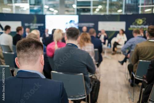 Focused shot of attendees at a business conference. The discussion panel is blurred in the background, highlighting engagement and learning.