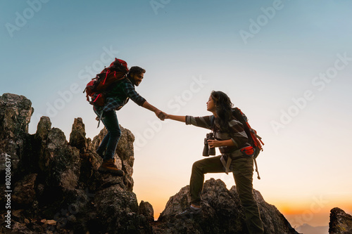  man and a woman are helping each other climb a mountain © lovelyday12