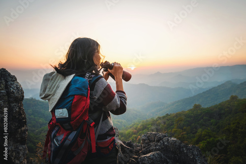 Female tourist on top of mountain use binoculars to view mountain range at sunset © lovelyday12