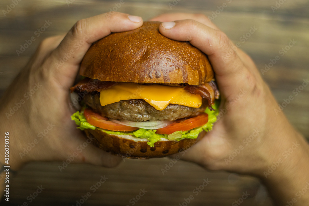 Duas mãos segurando um hamburguer em cima de uma mesa de madeira Two hands holding a burger on a wooden table 6 Duas mãos segurando um hamburguer em cima de uma mesa de madeira Two hands holding a burger on a wooden table 6