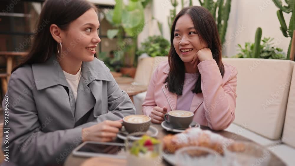 Two female friends, one Asian and one Caucasian, enjoying a brunch together at a cozy cafe, chatting over coffee and pastries. Two female friends, one Asian and one Caucasian, enjoying a brunch together at a cozy cafe, chatting over coffee and pastries.