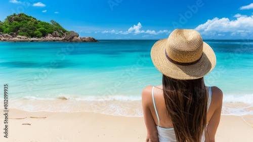 Woman in a summer hat relaxing on a pristine tropical beach, looking at a turquoise sea. © red_orange_stock