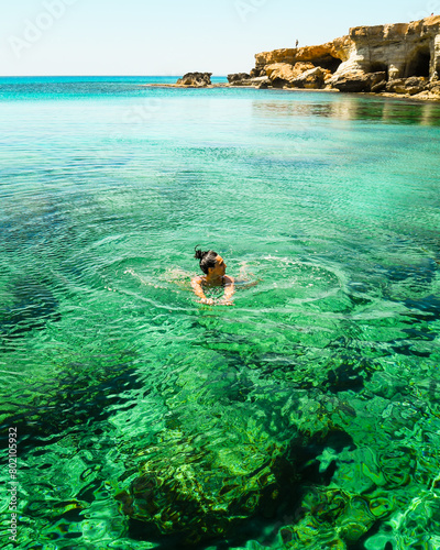 Woman swims in Northern cyprus Ayia napa bay shore with crystal clear blue mediterranean waters and tranquil seascape and rocky stone shore. Sea caves popular travel destination photo