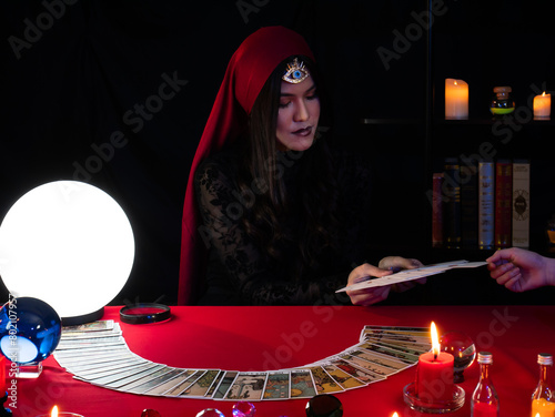 A serious fortune teller with tarot cards in hand for customer choose for reading the future by candlelight with a glowing orb adding to the ambiance